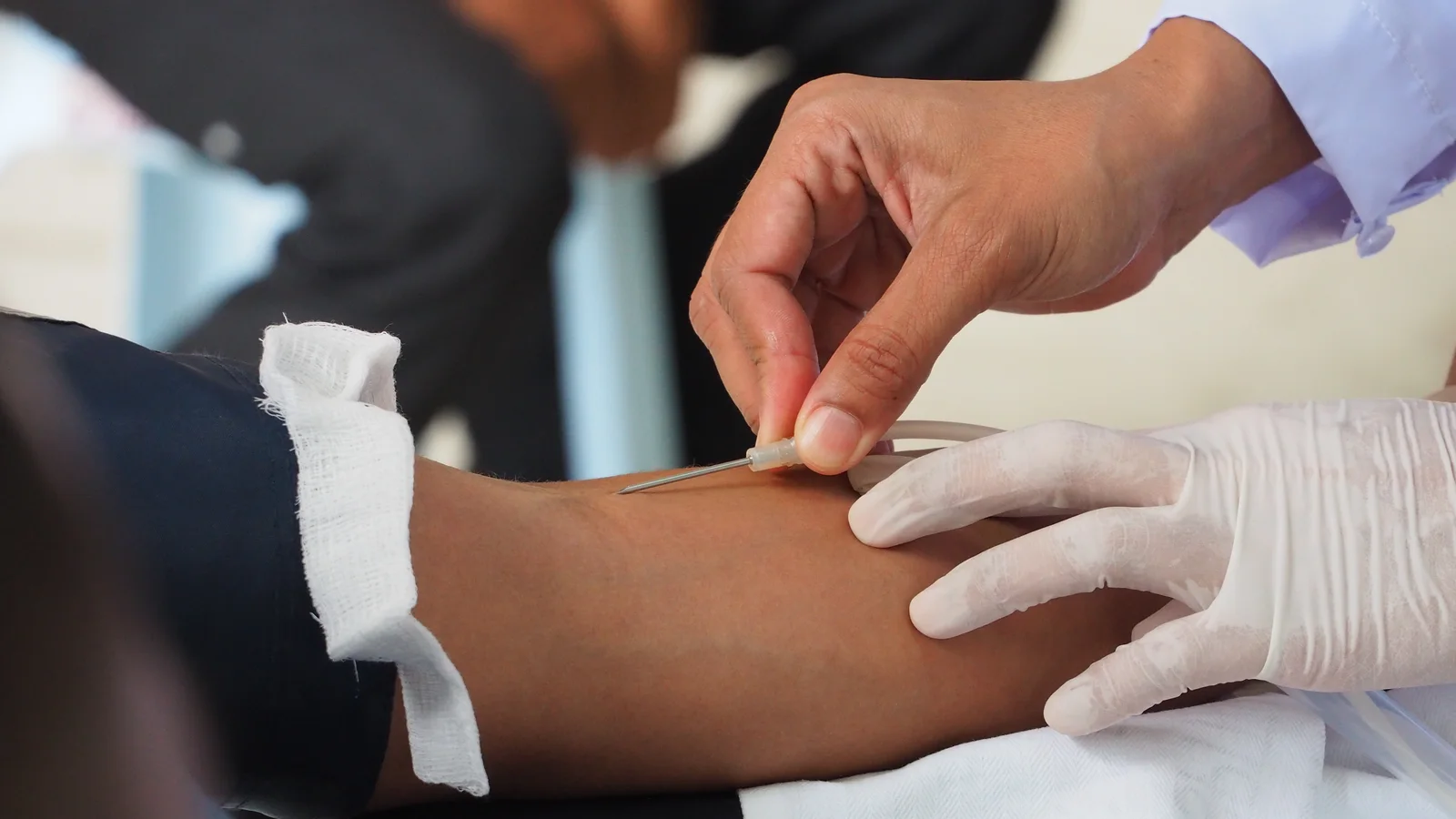 A close-up of a blood sample being drawn from a patient's arm by a gloved clinician
