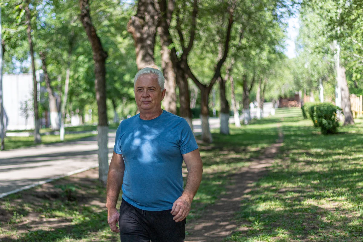 A grey-haired man in his sixties walking at pace along a tree-lined park path in a blue shirt