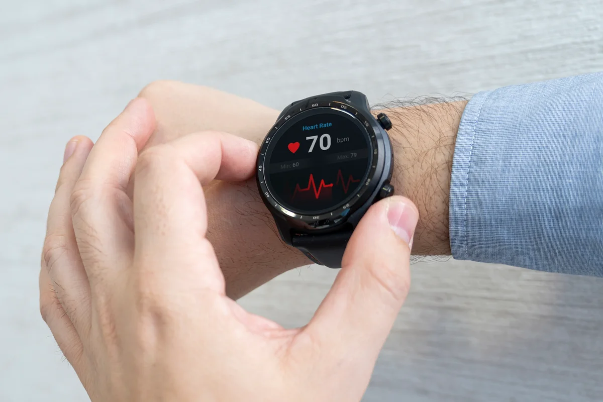 Two hands and a shirt cuff, checking a smartwatch that reads 70 beats per minute with a trace
