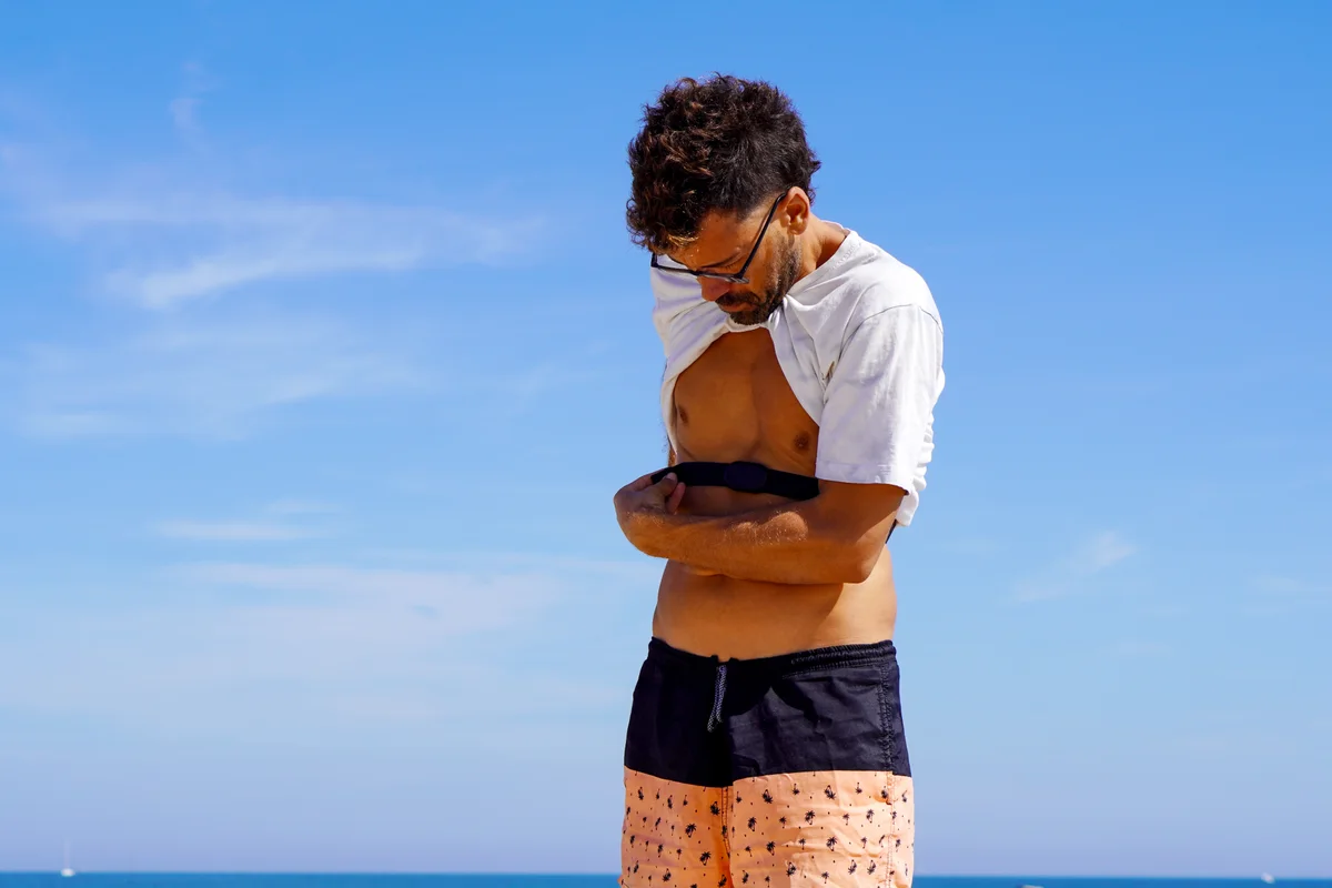 A man fitting a heart rate monitor chest strap around his chest before a run outdoors