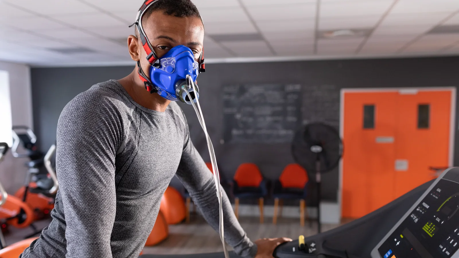 A man mid test on a treadmill, breathing through a blue gas mask wired to the analyser